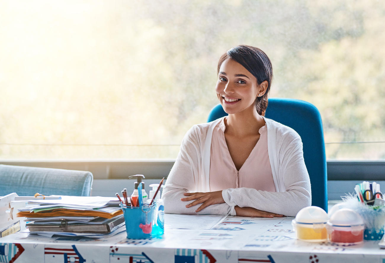 Welcome to the teacher homepage. A similing teacher sits at her classroom desk.