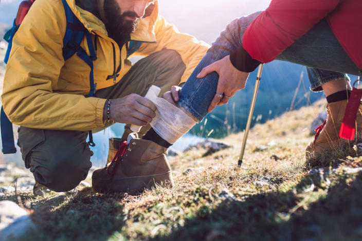 A hiker getting first aid from another hiker in the mountains.